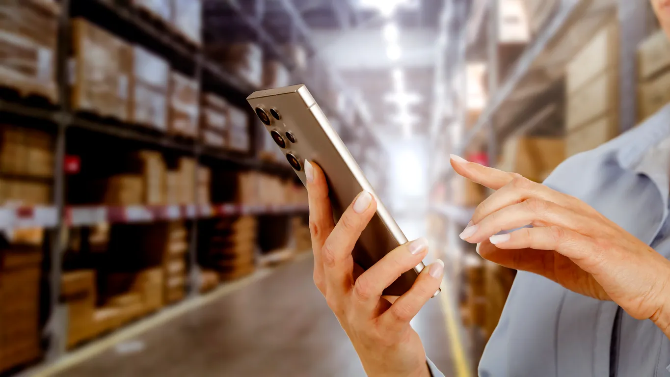 Manos de persona usando un celular inteligente, dentro de un almacén con multiples productos al fondo