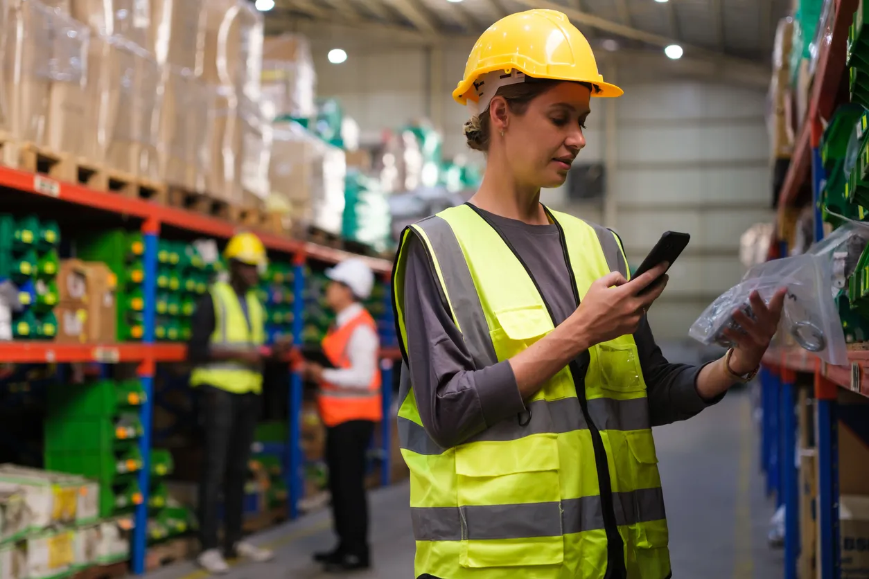 Mujer trabajadora en almacén revisando datos en su celular. Los celulares XIAOMI son resistentes en estos ambientes