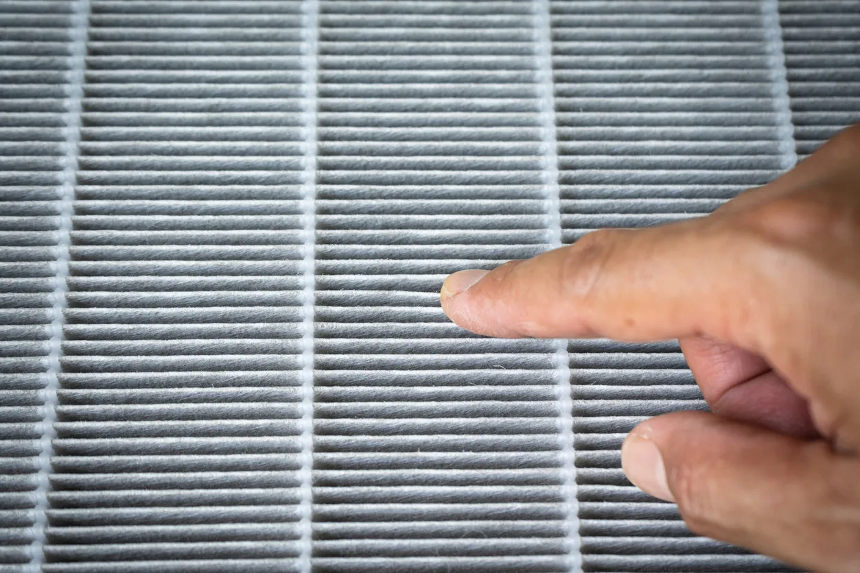 Primer plano de un filtro purificador de aire (filtro HEPA) con polvo. Una mano señala el polvo con el dedo.