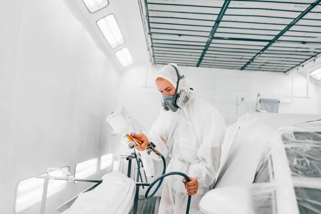 Hombre trabajando en servicio profesional de pintura de automóviles, con un sistema de filtración en el techo.