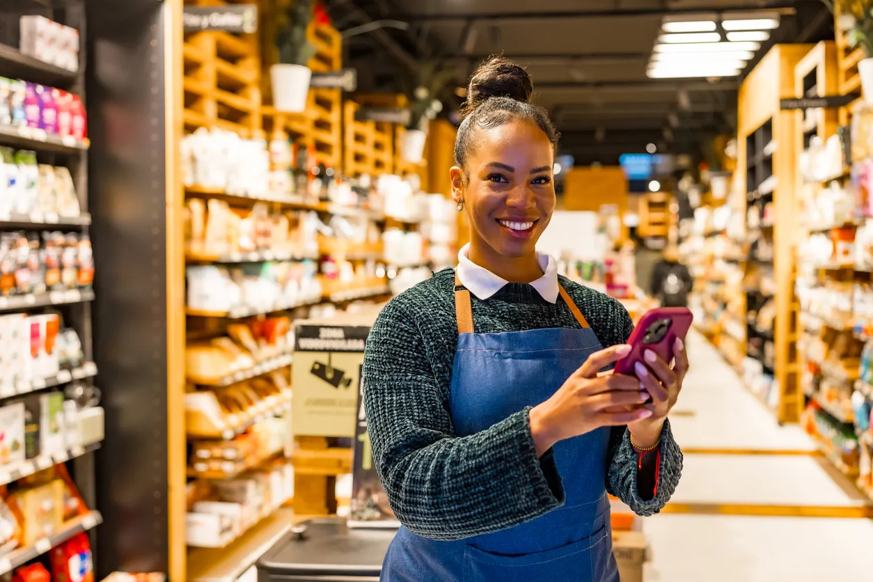 Vendedora sonriente usando celular en un supermercado. Los celulares de media gama son adecuadas para estas areas