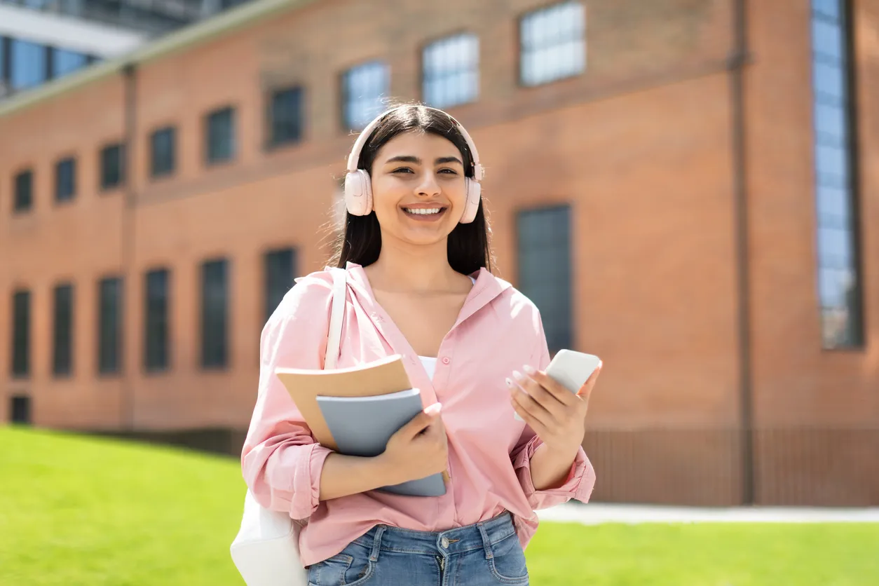 Estudiante moderna. Mujer latina feliz con cuadernos y teléfono celular de media gama, disfrutando de la música