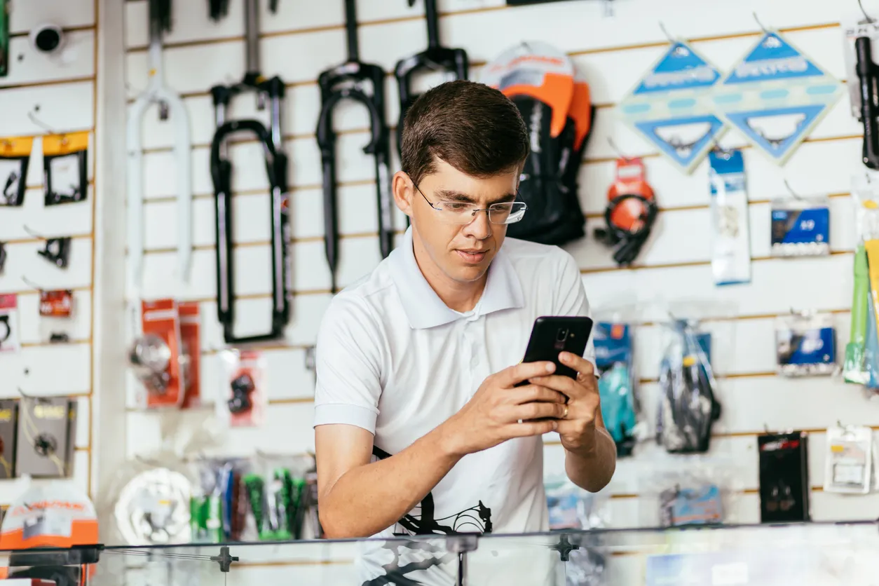 Dueño de una tienda de bicicletas trabajando en su taller revisando se celular de media gama.