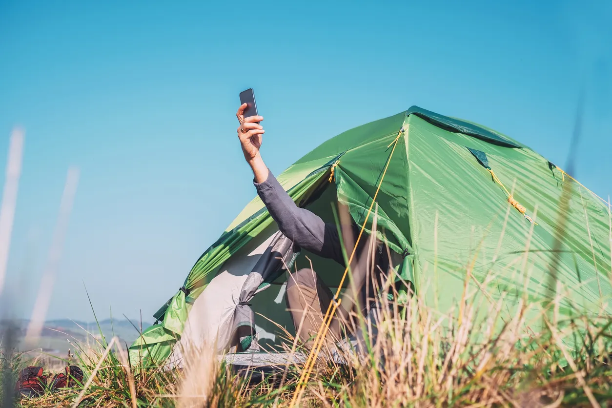 Un viajero se sienta en una tienda de campaña turística e intenta captar la red celular.