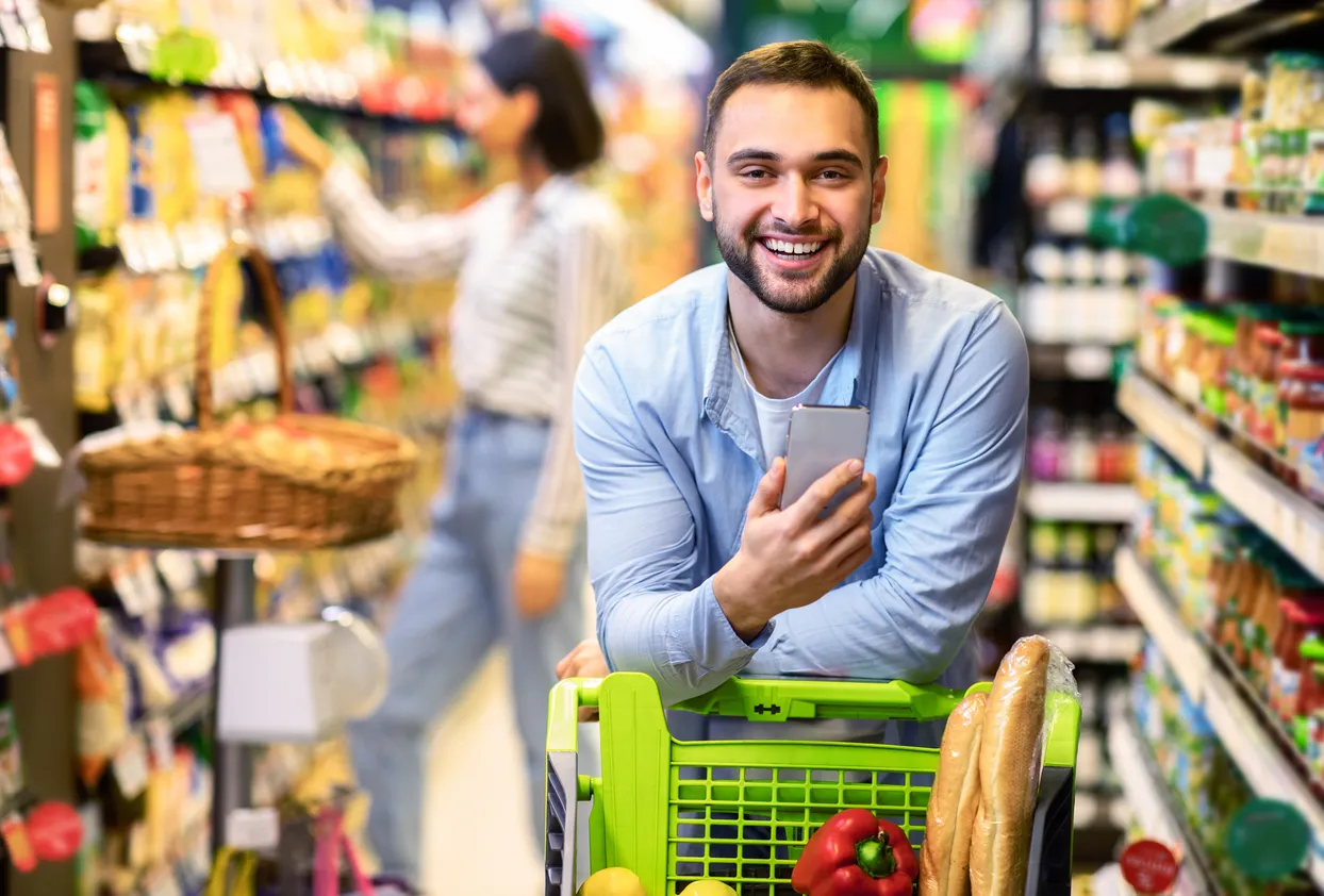 Chico joven con teléfono móvil de media gama comprando en un hipermercado