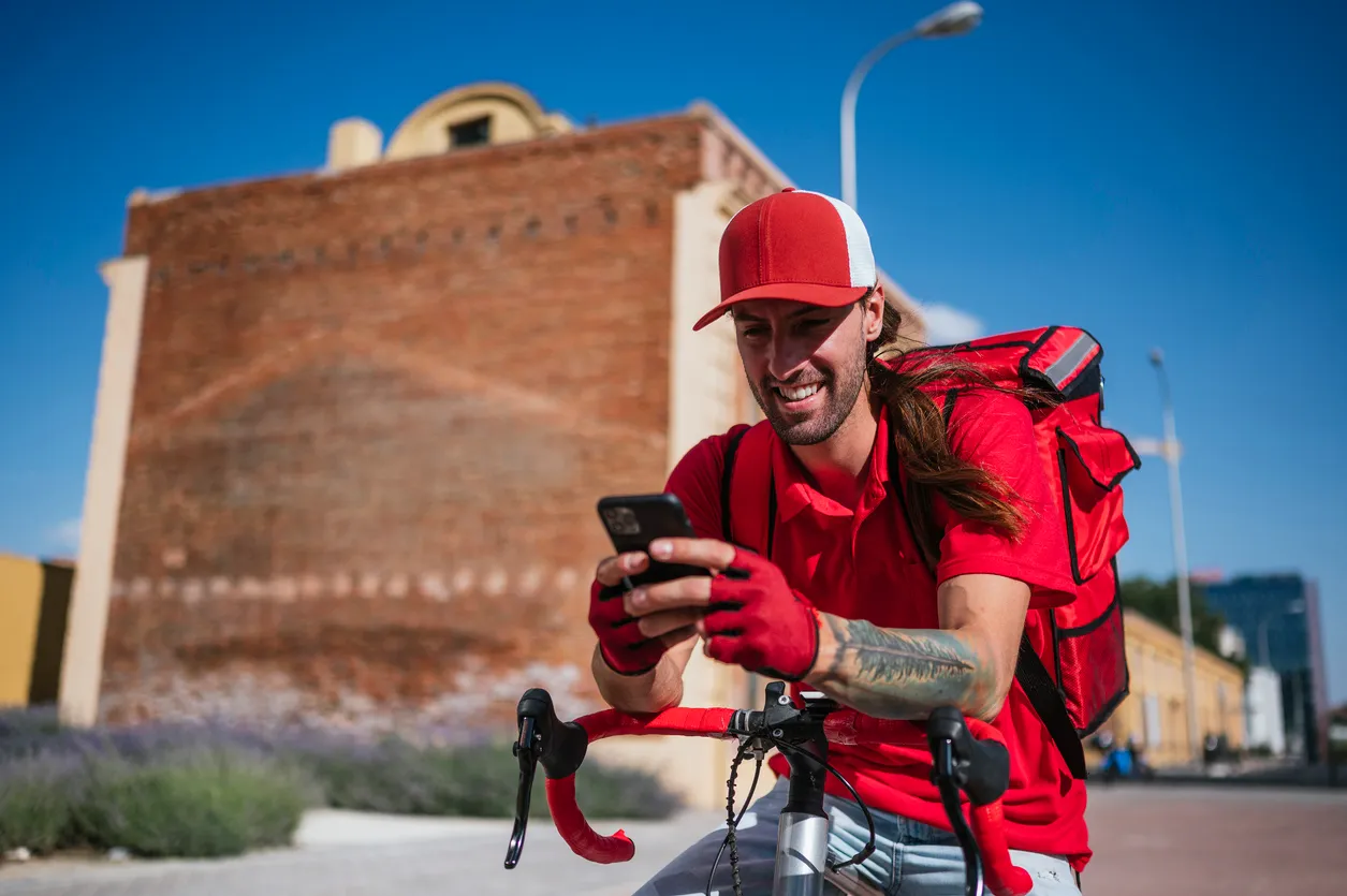 Hombre que trabaja repartiendo comida por mensajería a domicilio consultando el teléfono inteligente de media gama