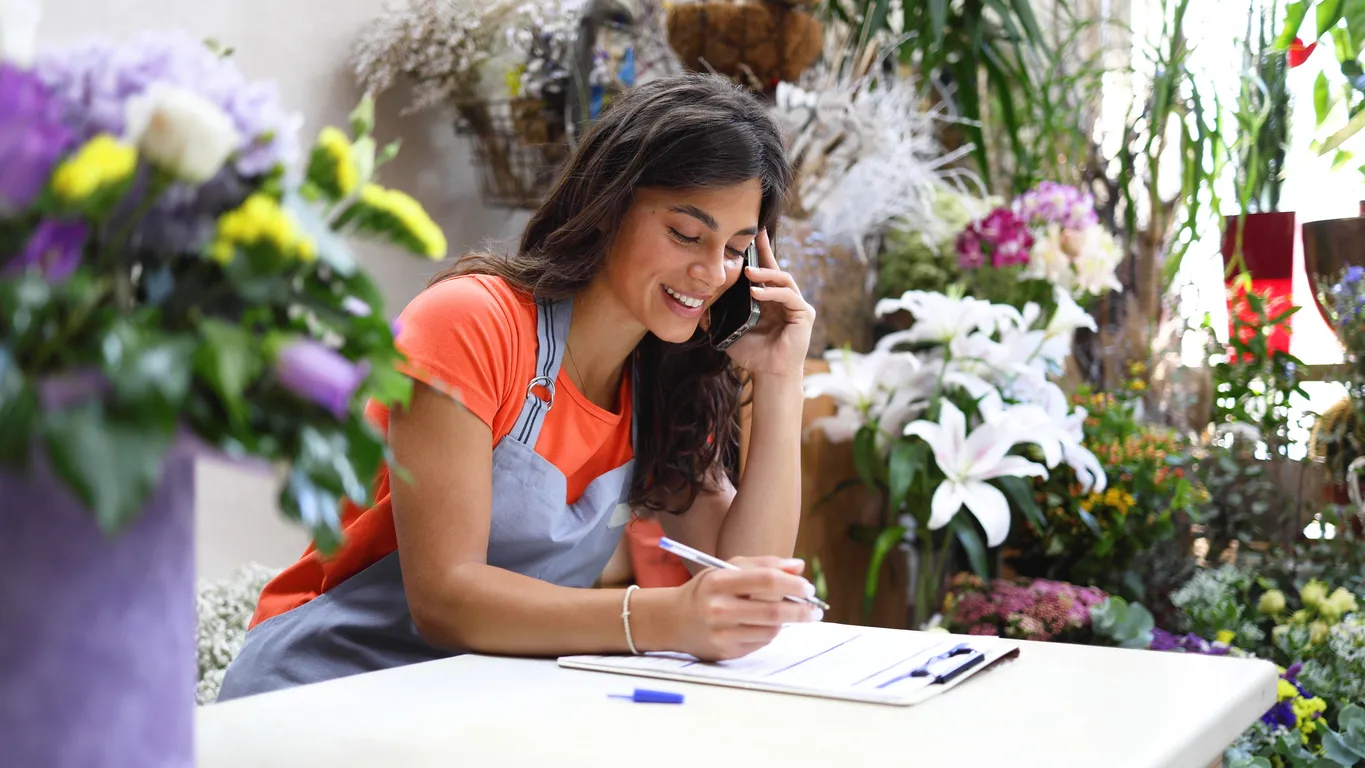 Propietaria de una floristería gestionando su negocio usando una smartphone de acuerdo a lo requiere.
