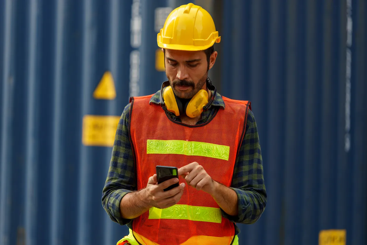 Oficial caucásico. Use ropa de seguridad reflectante. Use casco de seguridad. De pie, usando el teléfono móvil