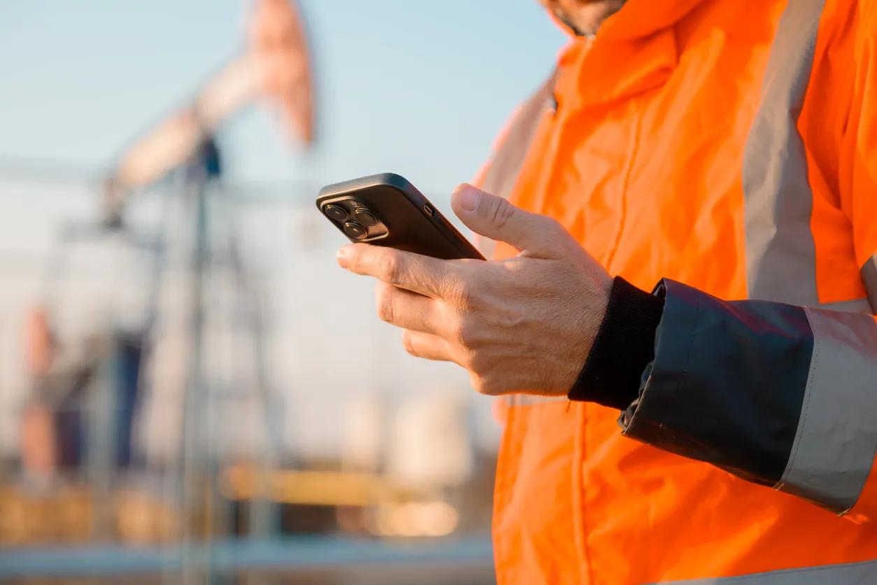 Ingeniero de plataforma de perforación que usa un teléfono inteligente mientras supervisa el proceso de petróleo y gas
