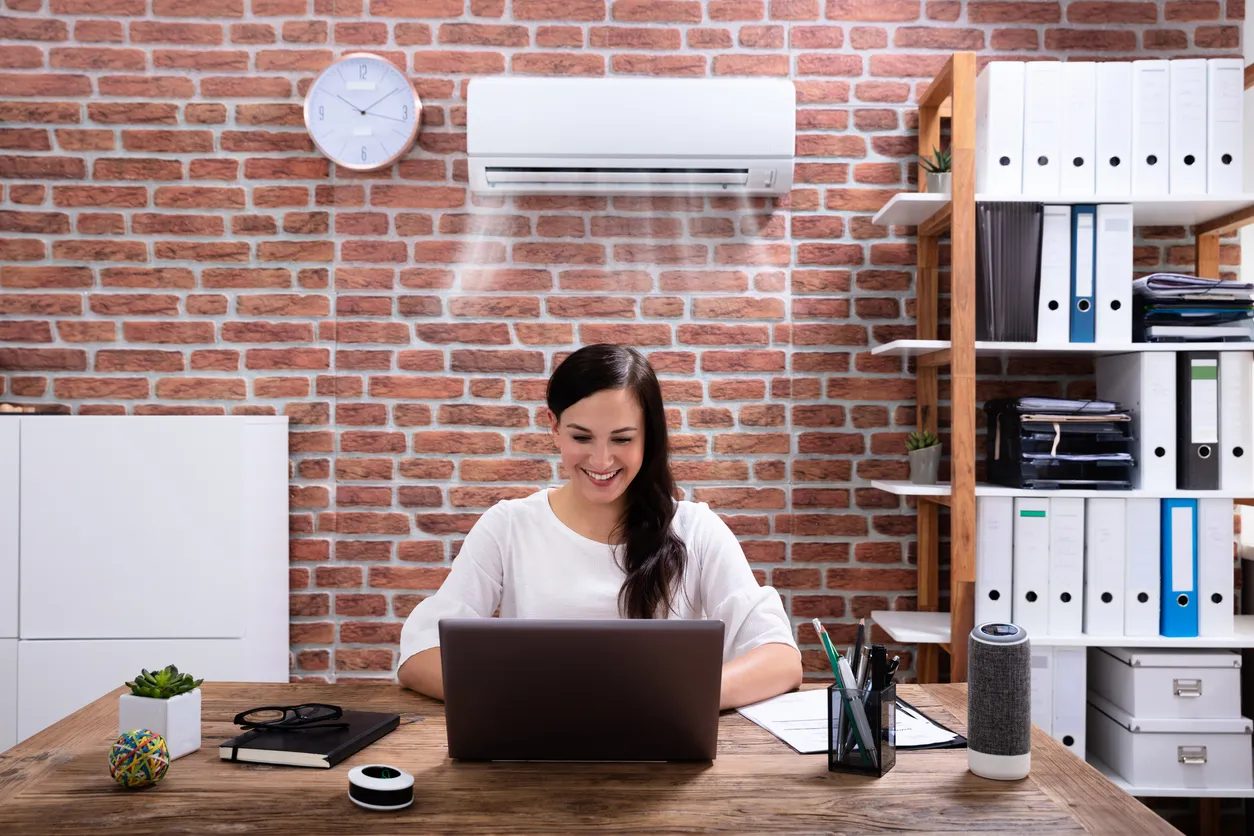 Mujer de negocios sonriente disfrutando del aire acondicionado usando una computadora portátil en el lugar de trabajo