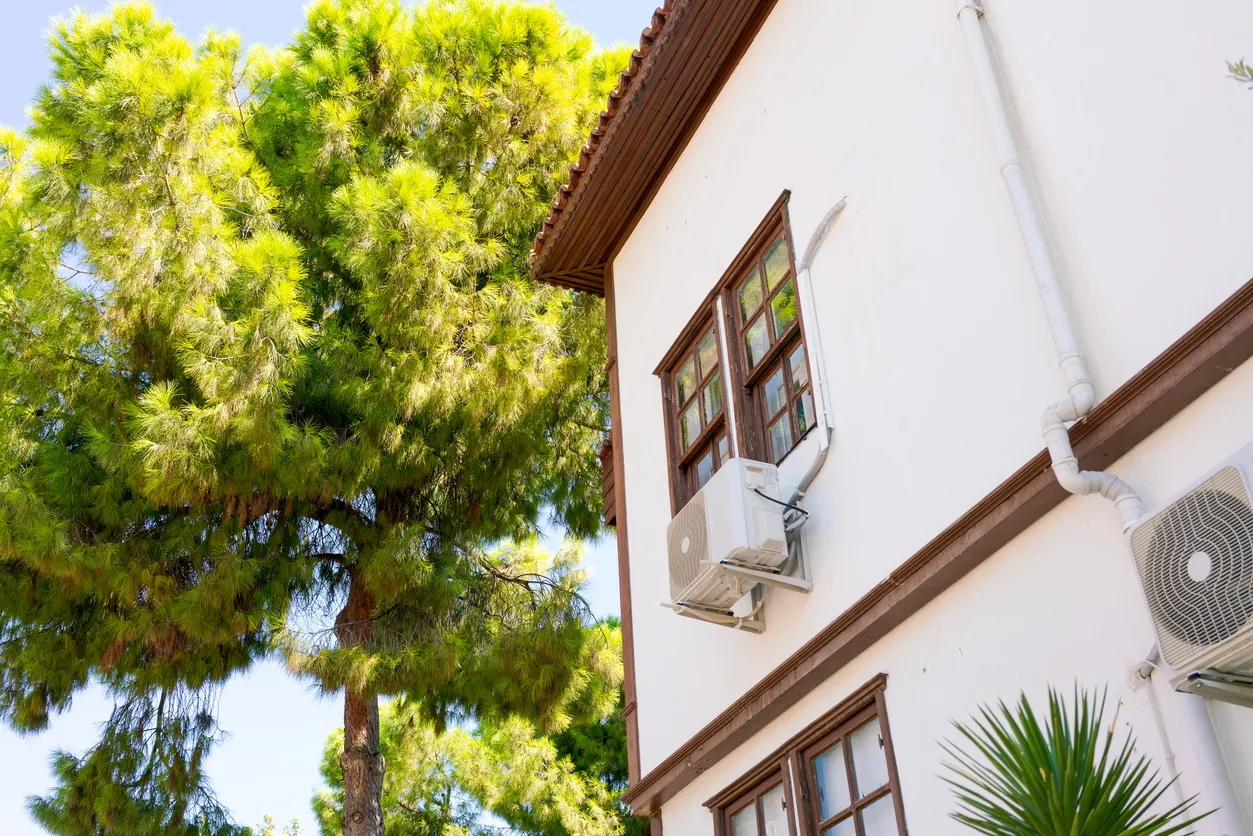 Casa con un árbol enfrente. La casa tiene una ventana con aire acondicionado.