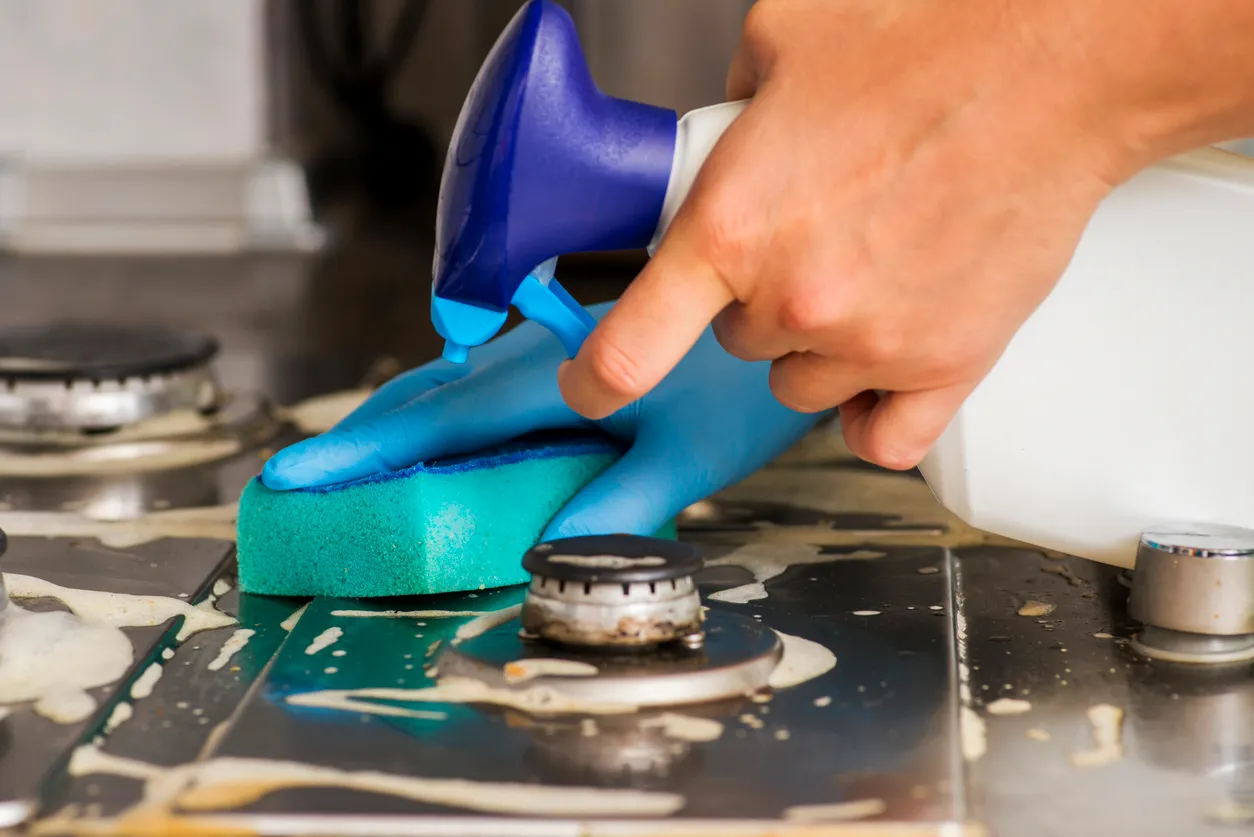 Mano femenina limpiando una estufa de gas con esponja y detergente. Limpieza de una estufa de gas con utensilios de cocina.