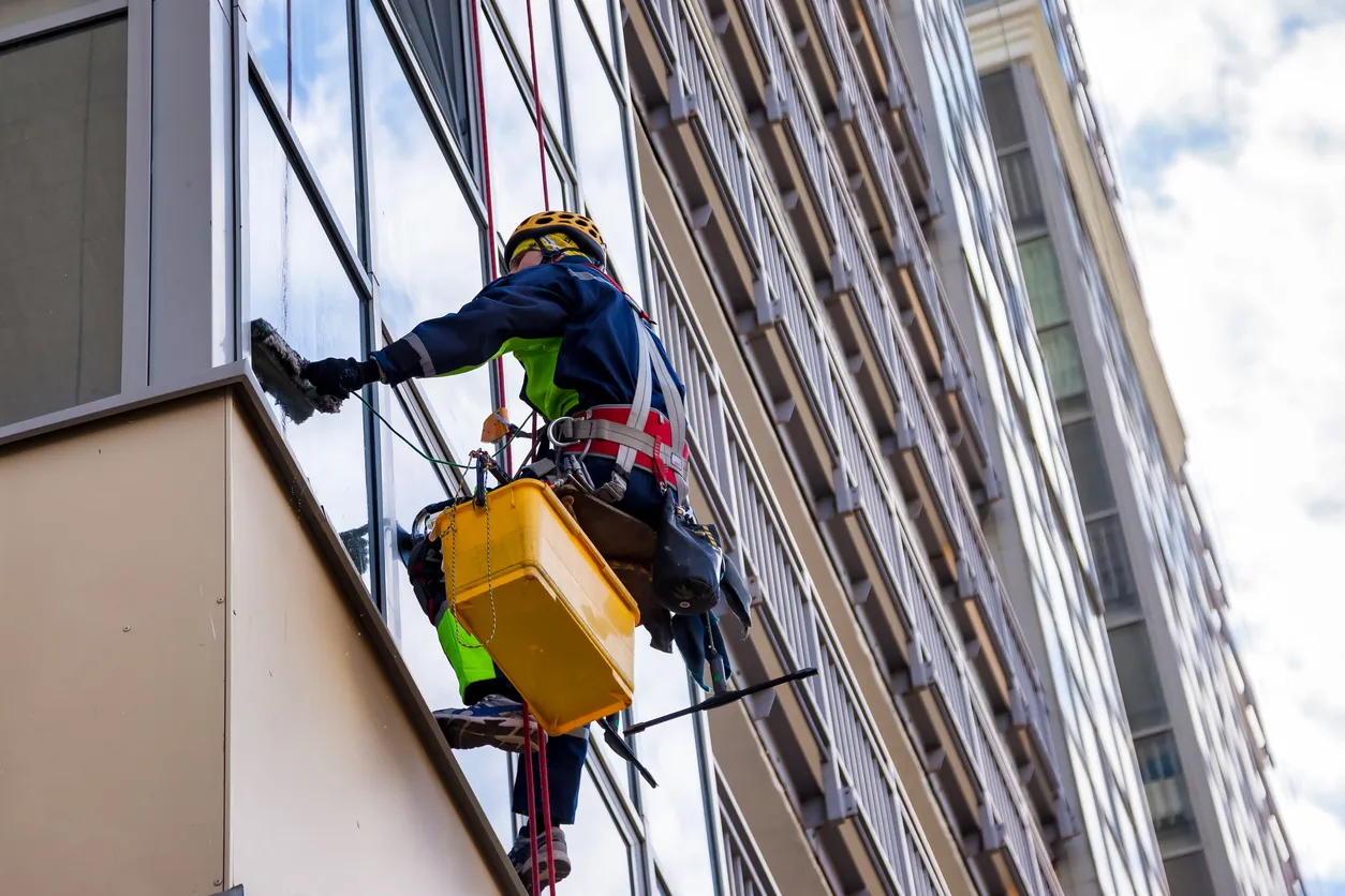 Trabajador industrial de alpinismo con uniforme lavando cristales, colgado de un edificio.