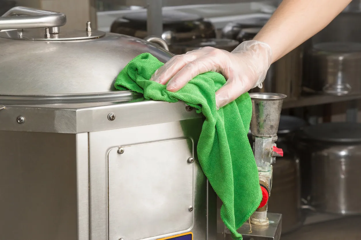 Mano en guante protector con trapo limpiando equipo de cocina en la cocina profesional