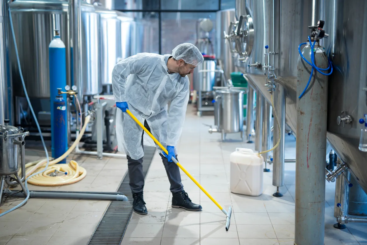 Hombre con uniforme de protección y cofia realizando limpieza en planta alimenticia