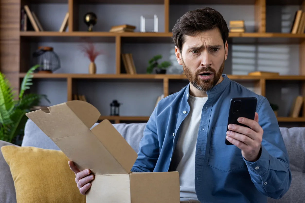 Un señor viendo su celular y con su otra mano agarrando su caja 