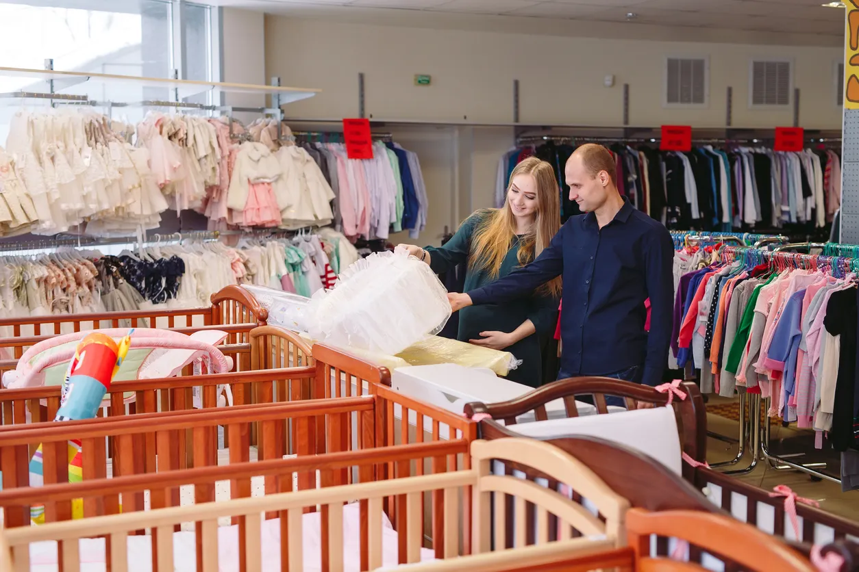 Parejo joven eligiendo accesorios y ropa de bebé en tienda 