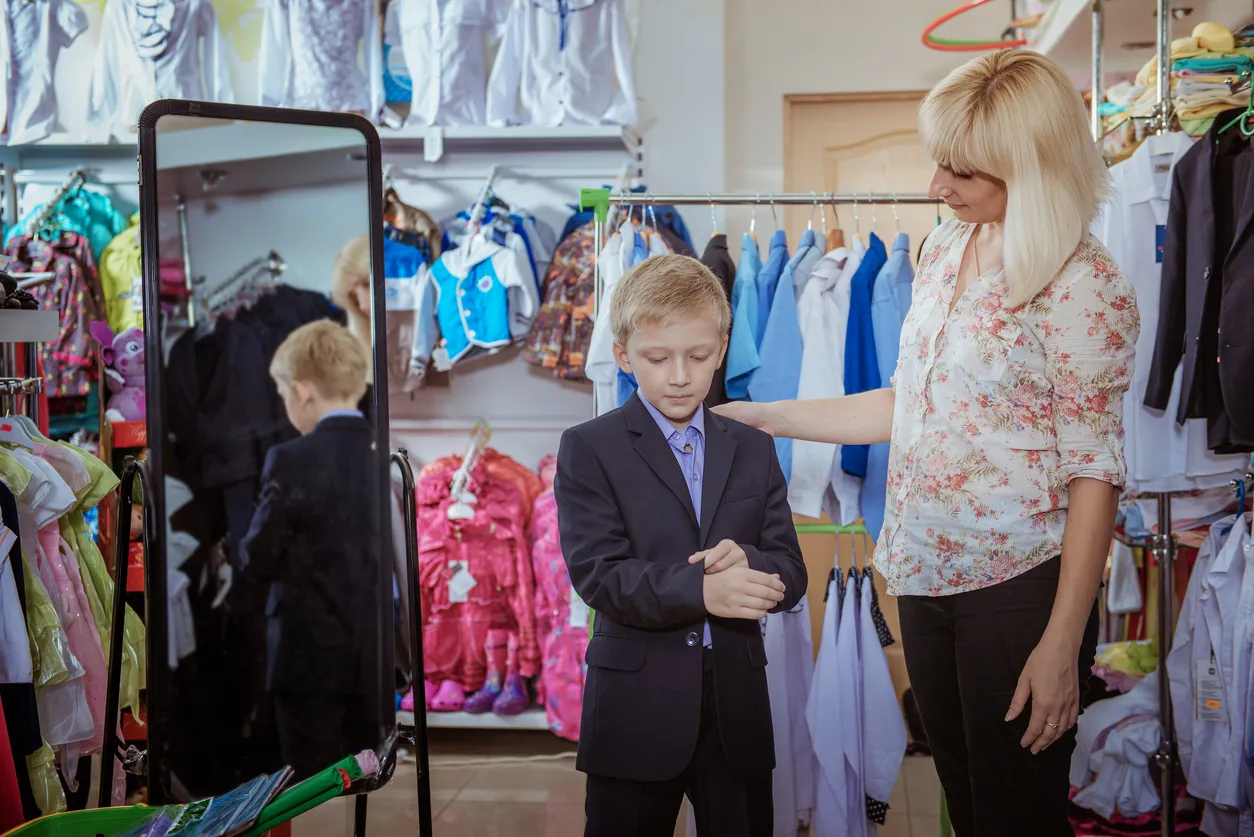 Niño probándose un traje con ayuda de su mamá en tienda de ropa para niños