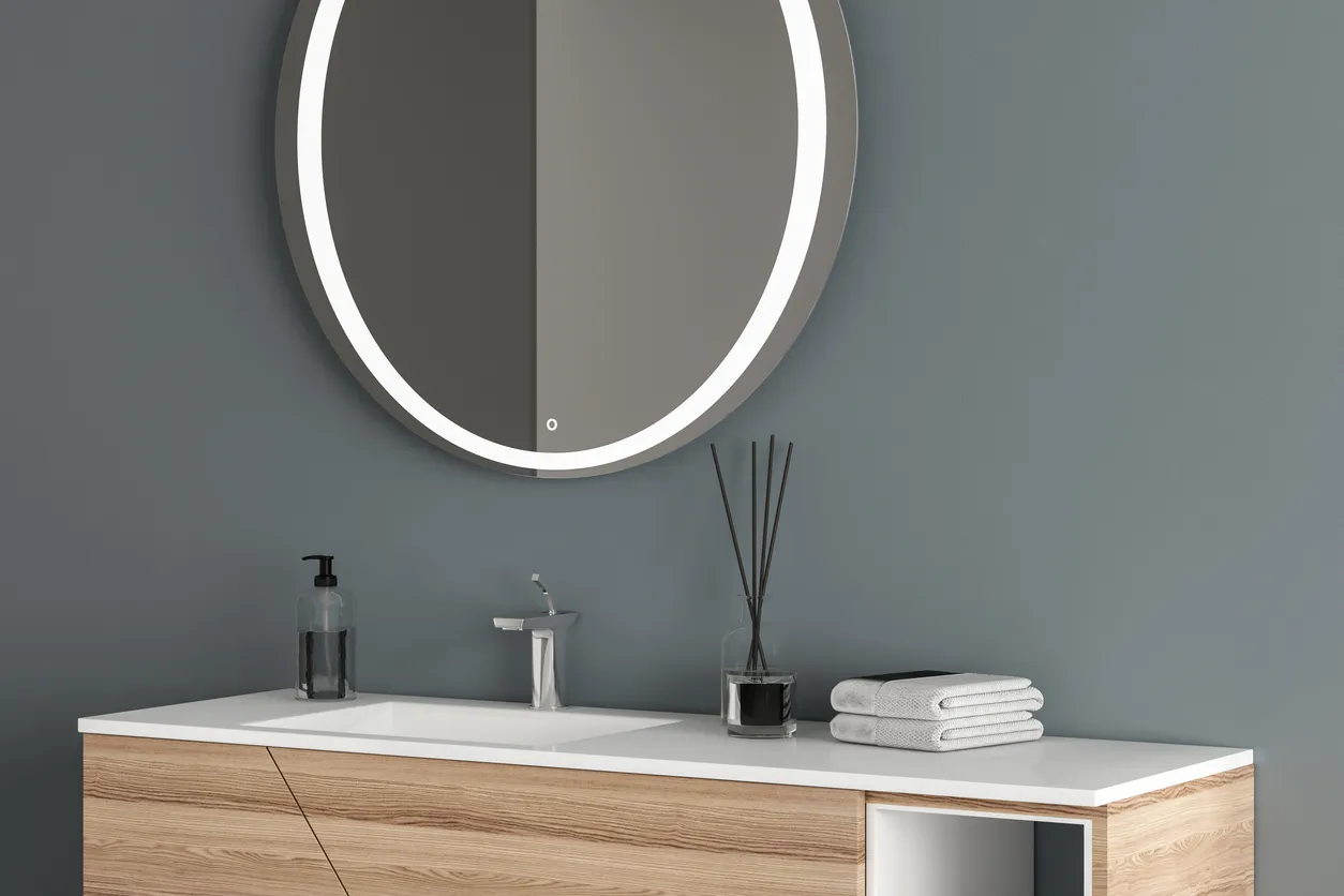 Lavabo blanco con espejo ovalado colgado en una pared azul, mueble moderno con grifo en un baño minimalista.