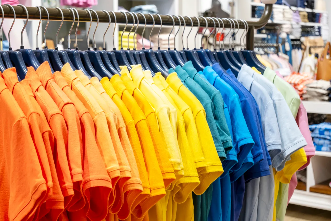 Gran catnidad de playeras polo de colores vivos en un exhibidor con ganchos.