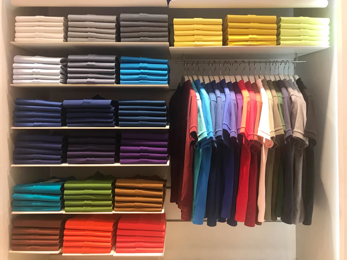 Gran catnidad de playeras polo de diversos colores tanto colgadas como dobladas por color en tienda de ropa 
