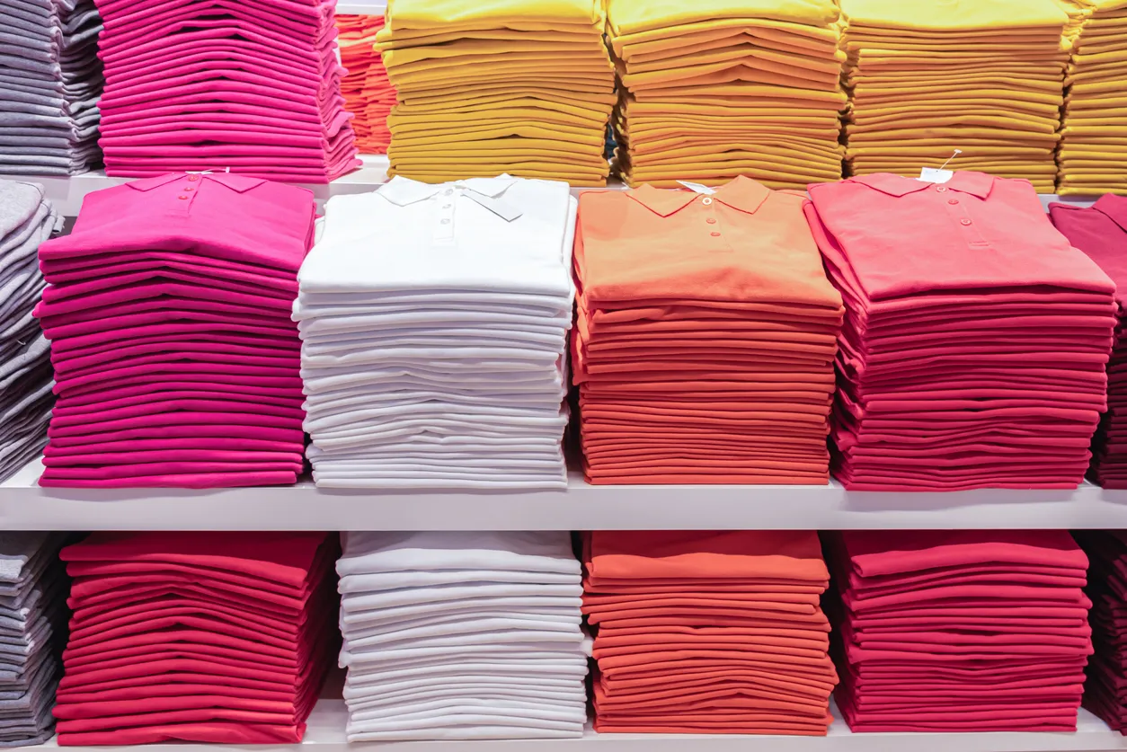 Se muestra un gran exhibidor de playeras en una tienda de ropa al mayoreo