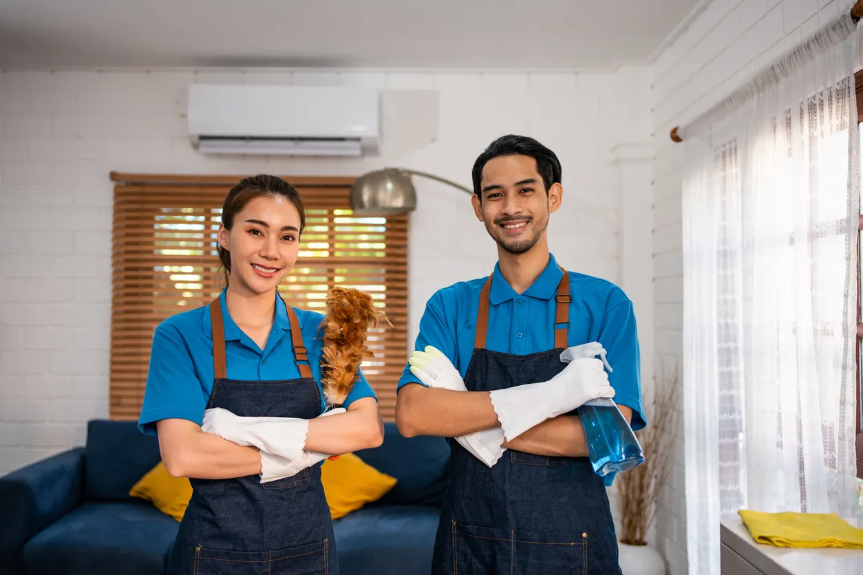 Dos jovenes con overoles y playeras azules y guantes blancas en la sala de una casa moderna