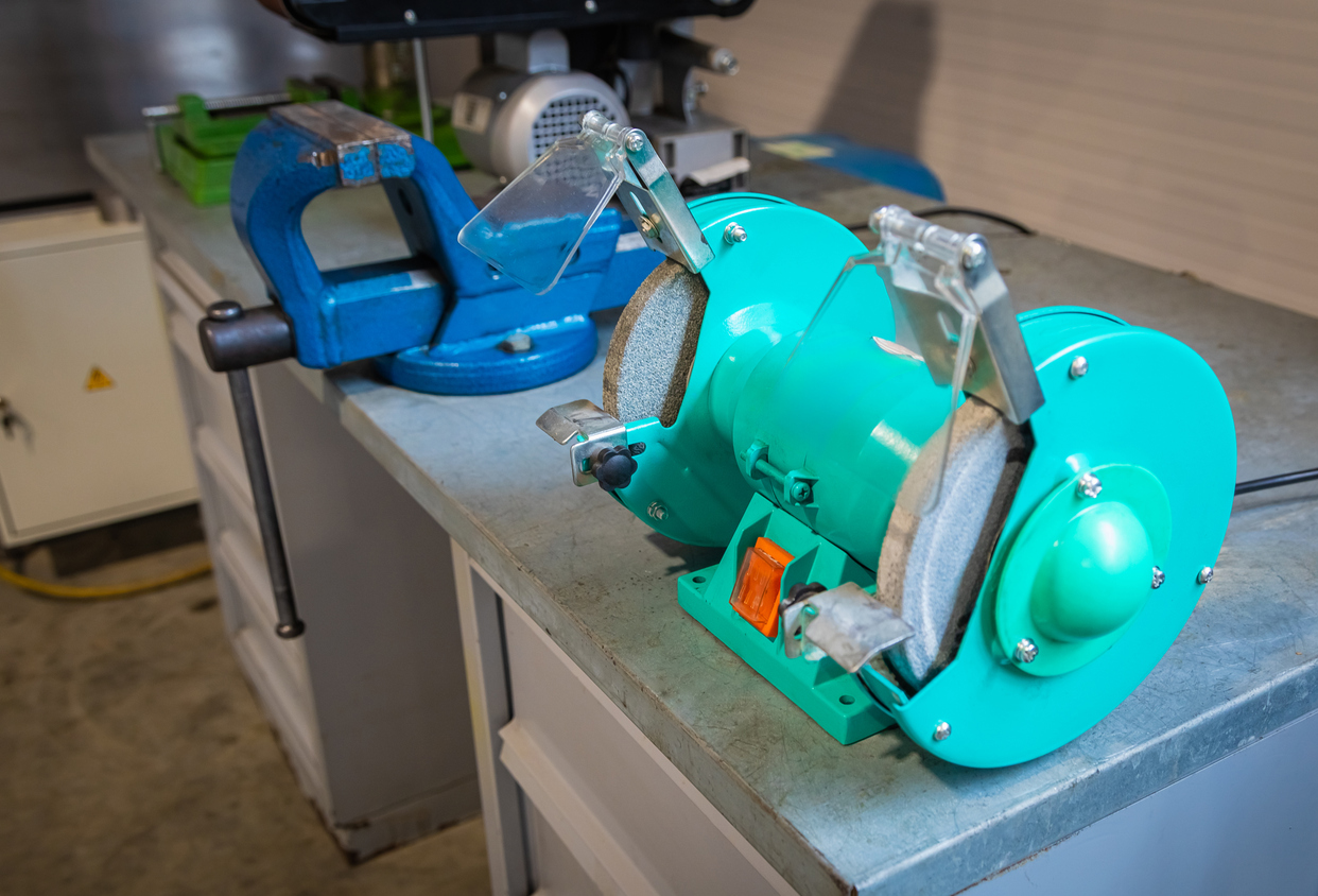 Amoladora de banco sentada en el banco de trabajo junto al tornillo de banco en el taller 