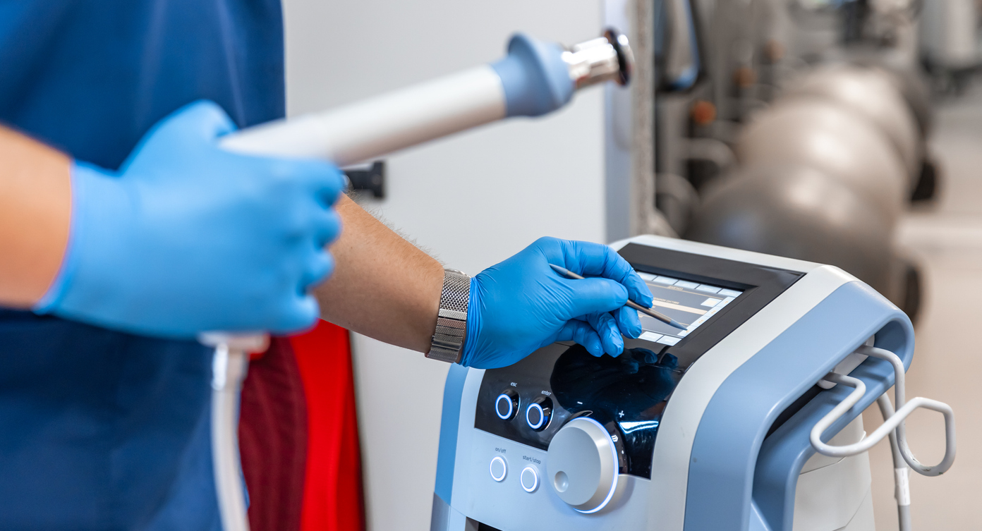 Dispositivo de terapia de ondas de choque con manos de médico masculino en guantes de goma.