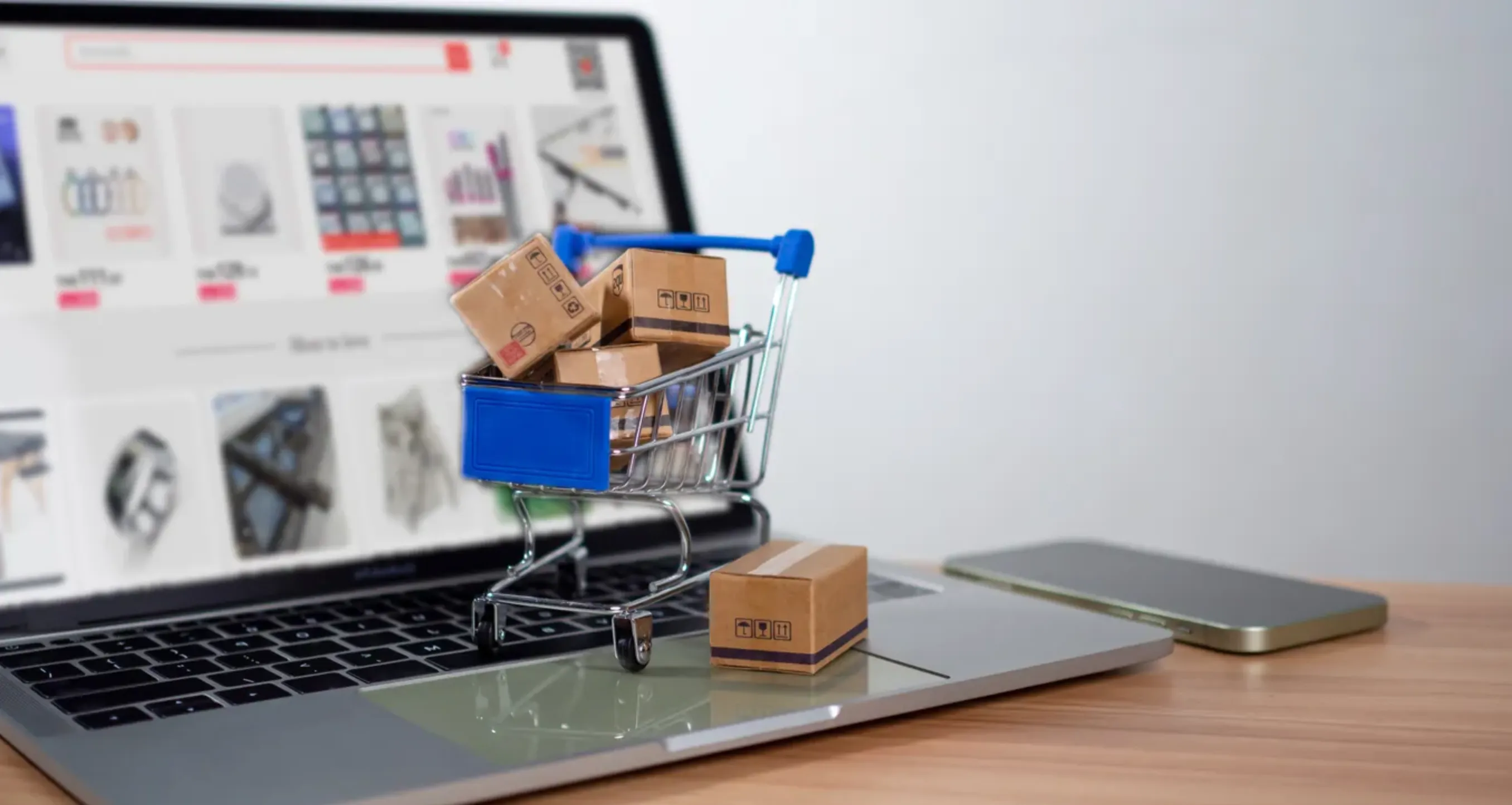 laptop con la pantalla en un marketpalce y encima de la laptop un carrito de compras de autoservicio con cajas de productos