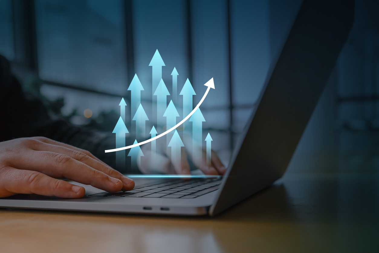 Una persona trabajando en una computadora portátil con una superposición digital de flechas brillantes hacia arriba y un gráf