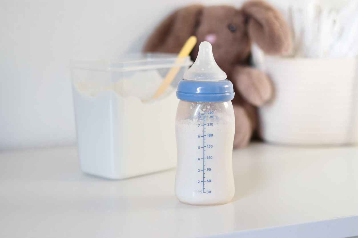 Un biberón con leche de fórmula para bebés en una mesa blanca, leche en polvo en polvo en una lata con una cuchara de plástic