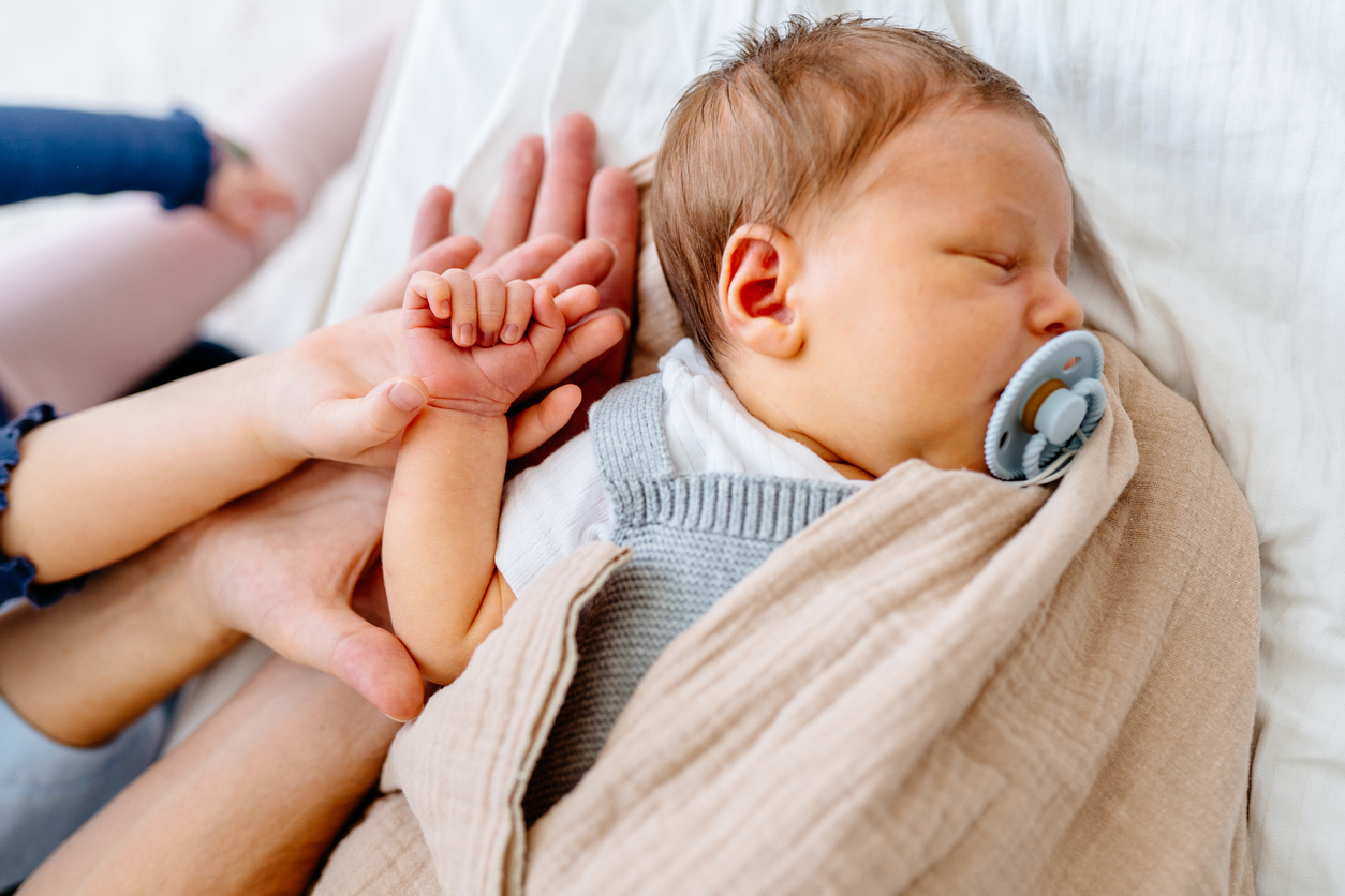 Bebé dormido de la mano del hermano con chupete y manta 
