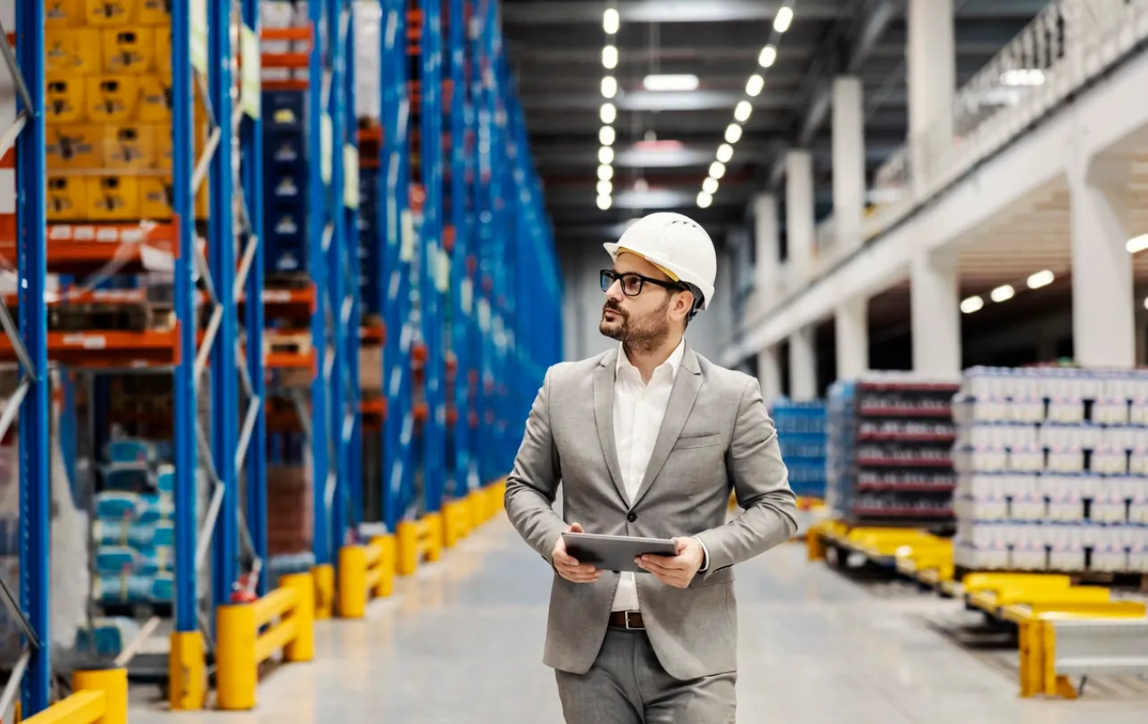 Hombre joven vestido formal y con casco de seguridad caminando en gran almacén de abarrotes
