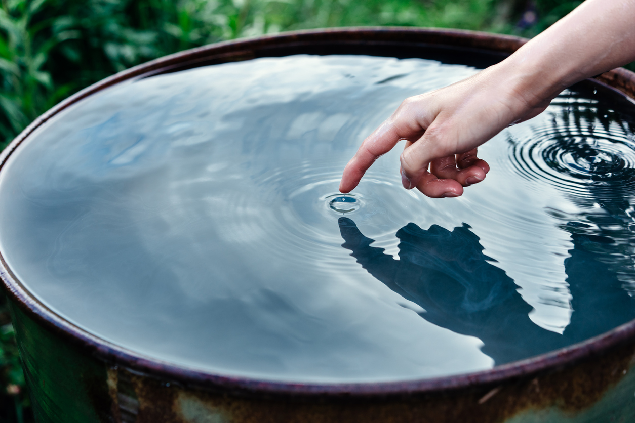 La mano femenina húmeda toca el agua limpia en un barril formando círculos en el agua 