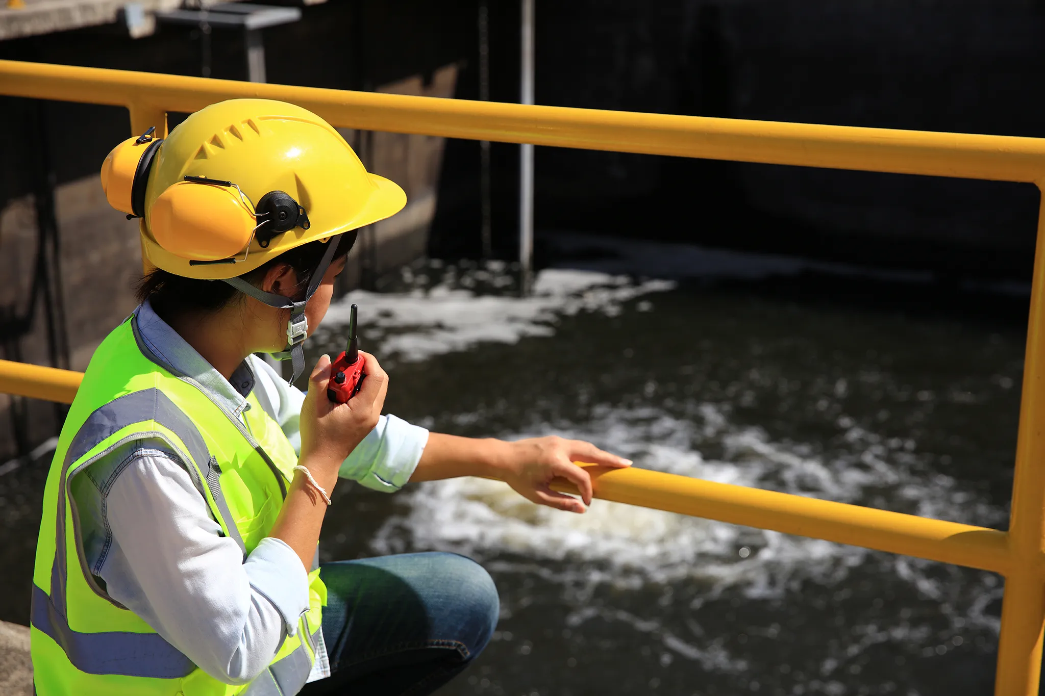 Mujer ingeniera con casco y radio de comunicación supervisando el proceso de tratamiento de aguas residuales
