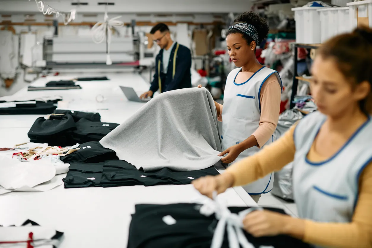 Empleadas en la fábrica textil que trabaja con tela en la línea de producción para uniformes de empresas