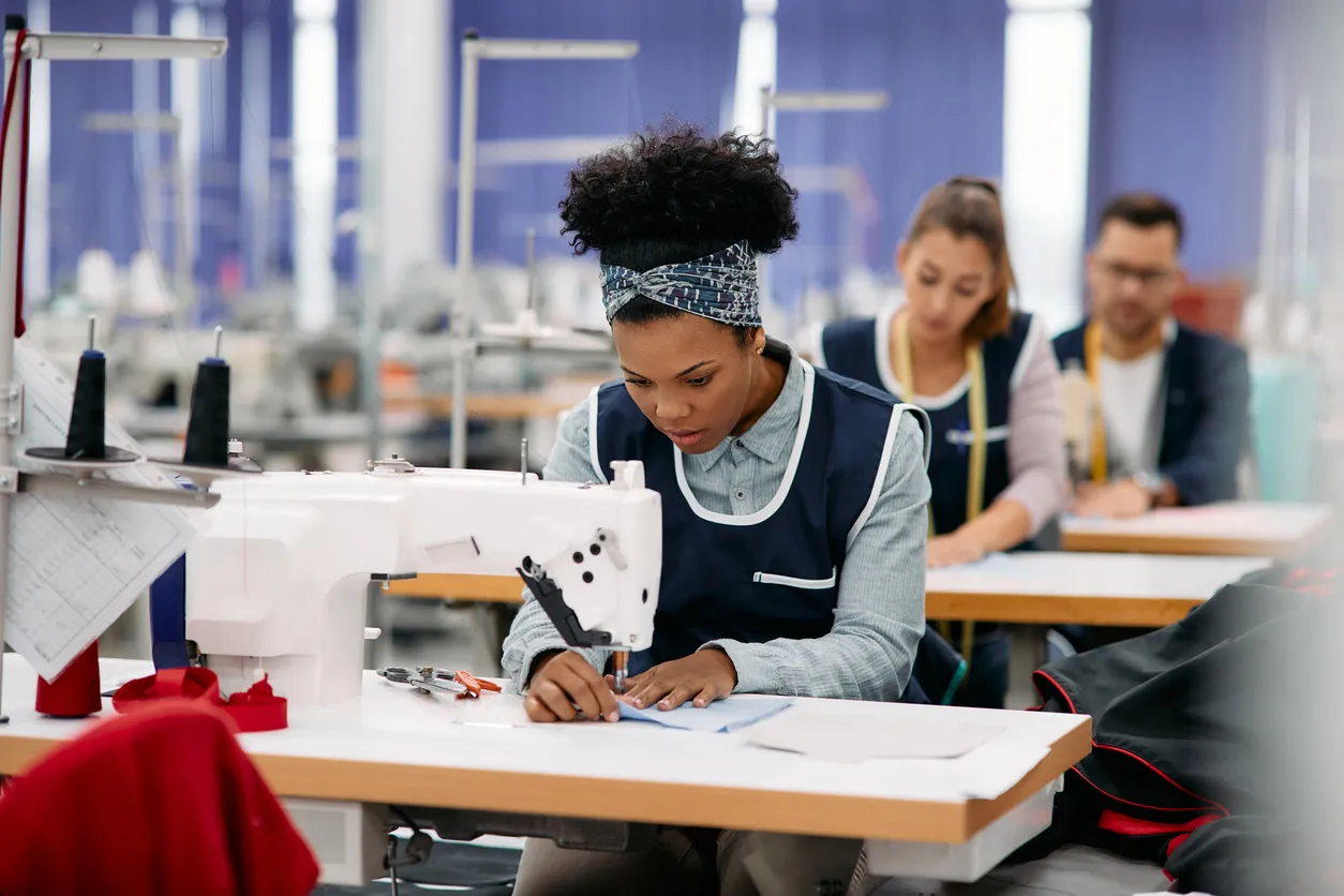 Joven trabajando como costurera en la línea de producción en una fábrica de uniformes