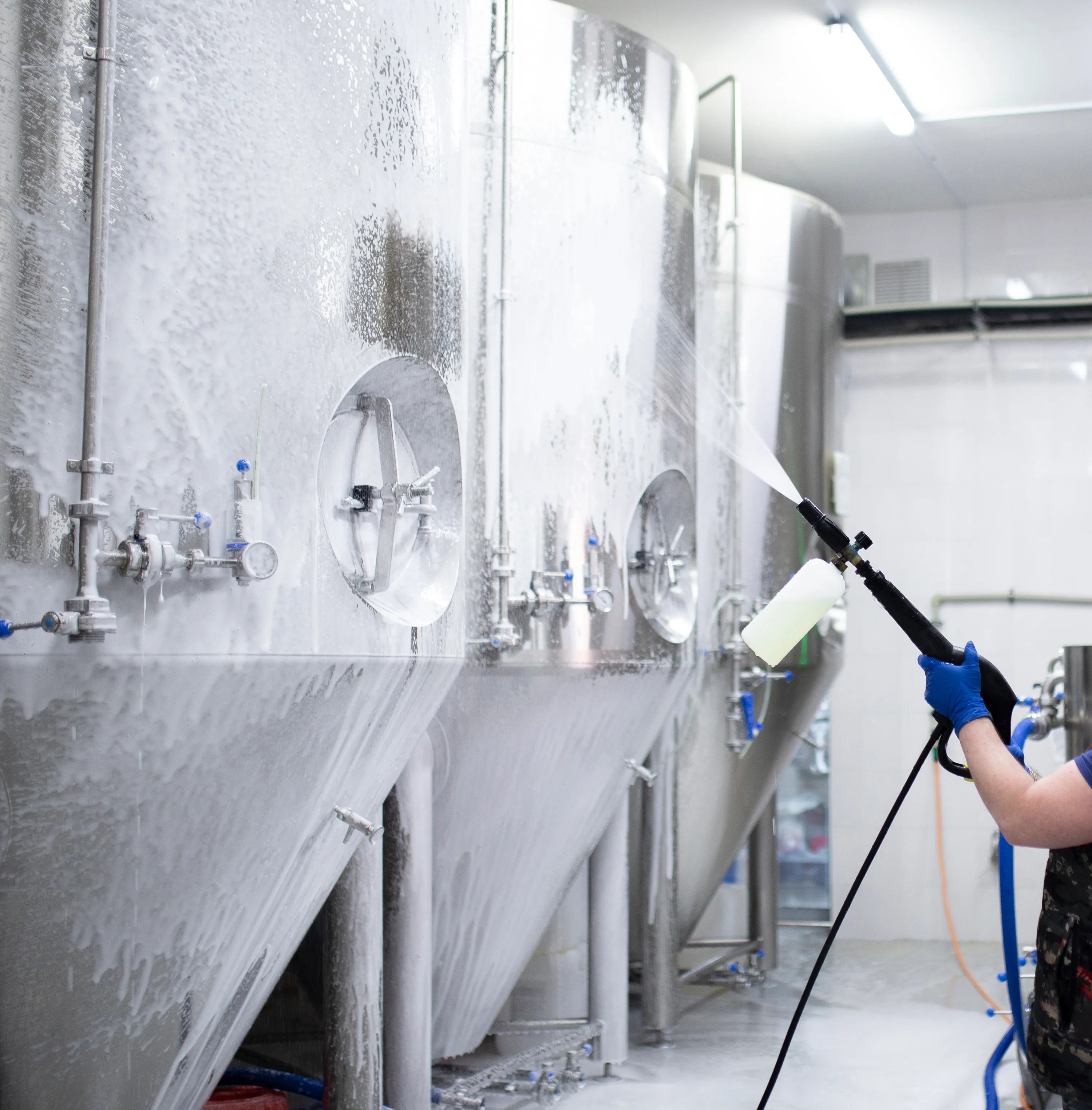 La mano del trabajador sostiene una pistola limpiadora de alta presión y pone espuma en el equipo de la fábrica