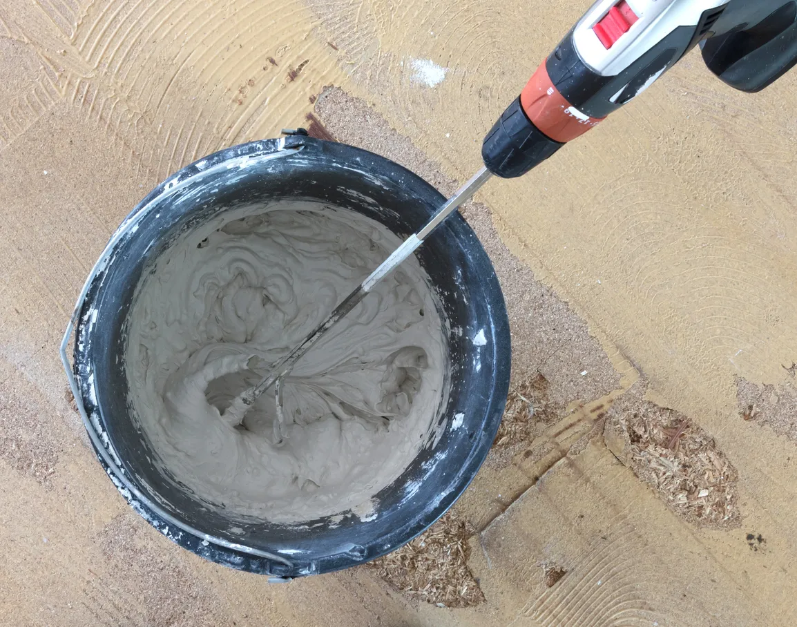 Un hombre sostiene un taladro mezclador en sus manos. Mezcla hormigón gris e imprimación en un cubo.