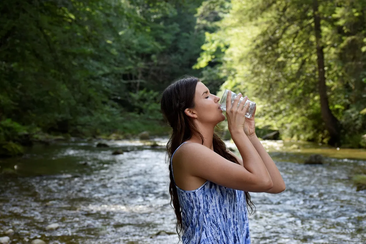 Mujer tomando vaso de agua. La importancia del agua para consumo humano
