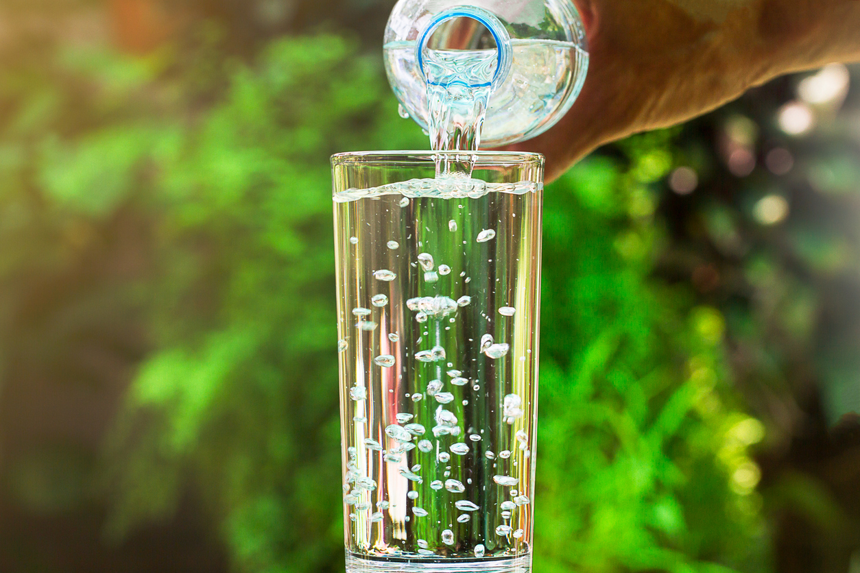 Cerca del agua que fluye de la botella de agua potable en vidrio sobre fondo jardín verde borroso, saludable beber concepto 