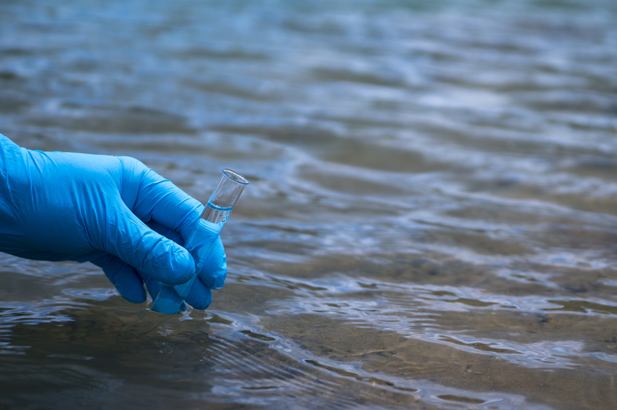 La mano de un hombre con un guante azul lleva un primer plano de agua a un tubo de ensayo para medir la contaminación del agu