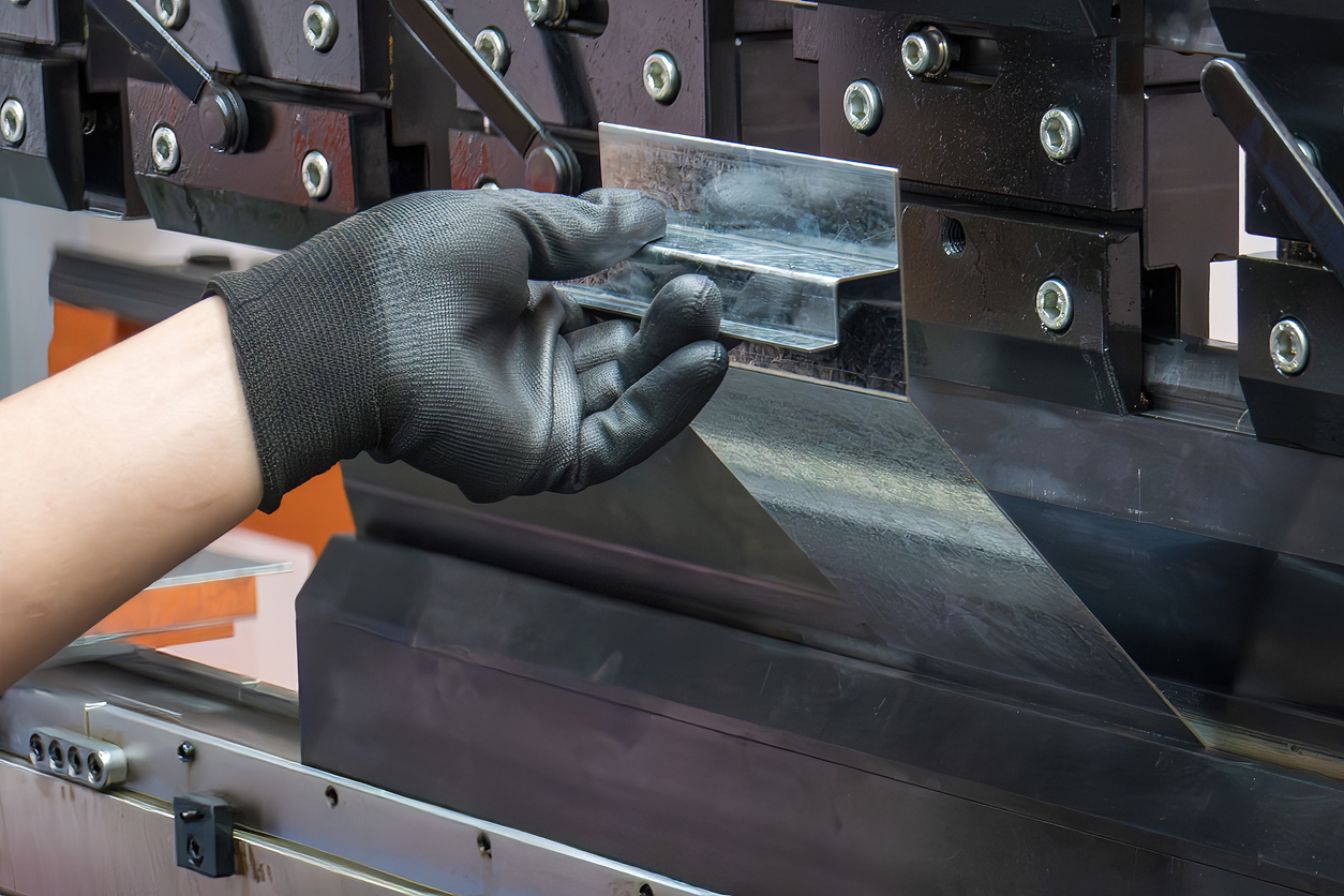 De cerca, el operador de la máquina dobladora sujeta las piezas de chapa metálica con un guante de goma. 