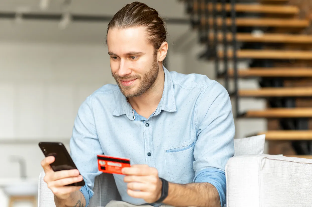 Hombre sosteniendo su celular inteligente en una mano y en la otra una tarjeta de crédito