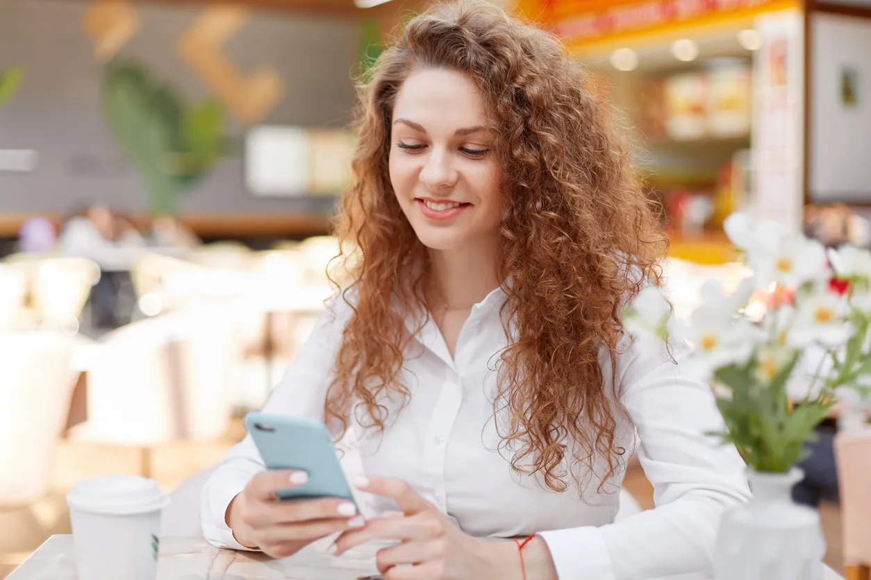mujer sonriendo revisando su celular de gama media