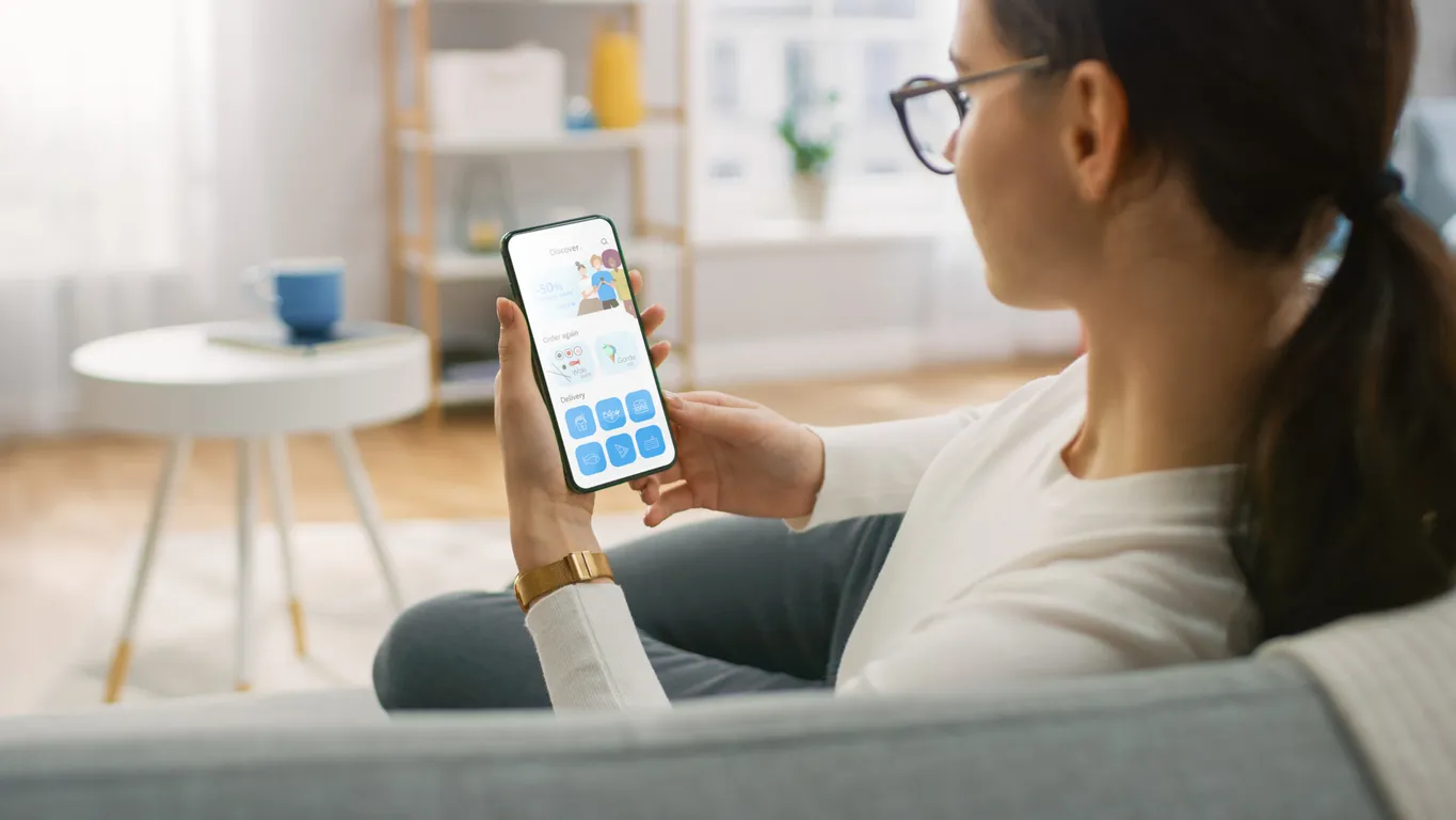 Mujer en una sala confortable viendo su celular. Los celulares baratos y teléfonos económicos los hacen accesibles a todos.