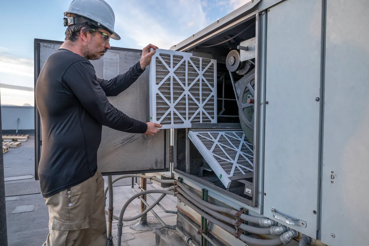 Mecánico de HVAC realizando un cambio de filtro de aire en una unidad de aire de reposición comercial