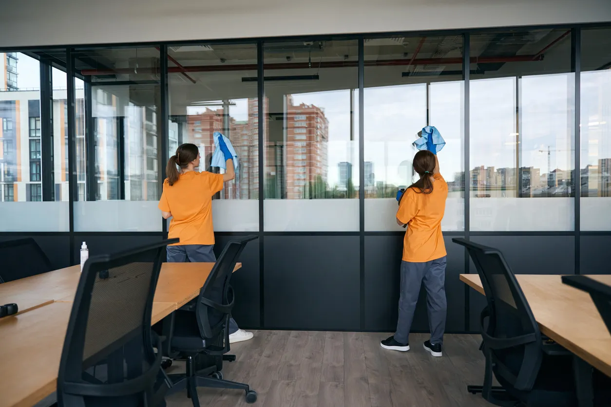 Dos empleadas de una empresa de limpieza lavan las ventanas de un espacio de coworking