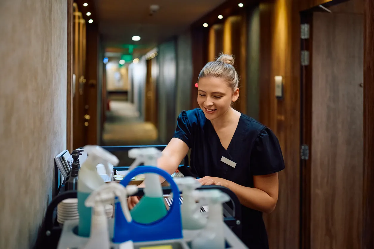 Mujer con carrito con productos de limpieza en el pasillo de un hotel.